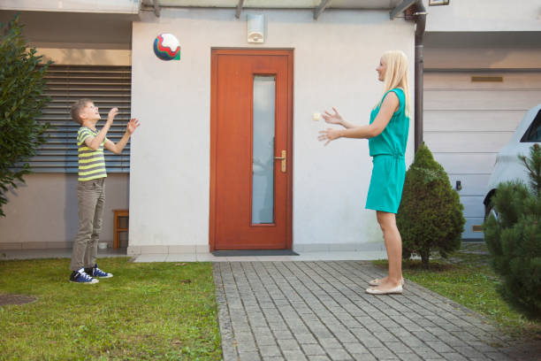 Mother and son throwing ball in front on their home. Front yard ball playing.