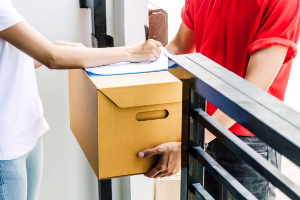 Woman putting signature in clipboard on cardboard box to receiving package with delivery man in red uniform.courier service concept stock photo