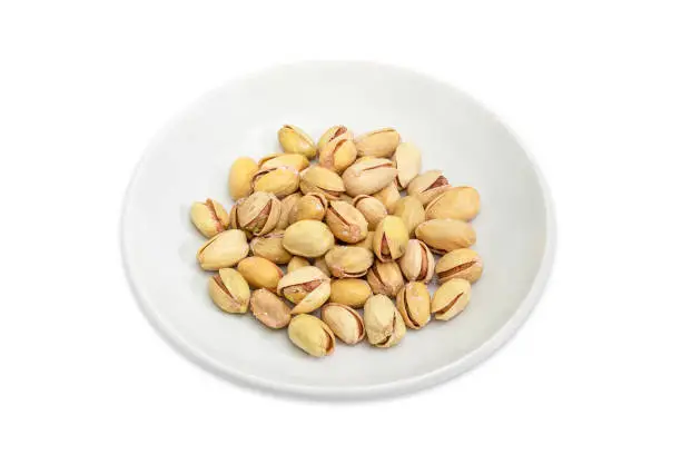 Roasted salted pistachio nuts with partly open shells on the white saucer on a white background