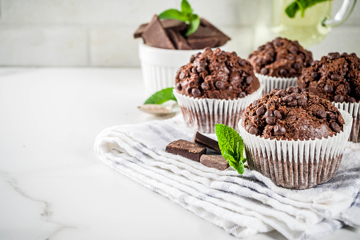Home baked mint and chocolate muffins with mint tea, white marble background copy space