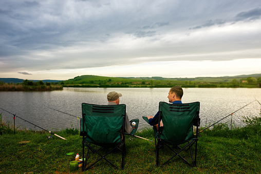 rear view of senior man with his son on fishing chairs enjoying relaxing moment.