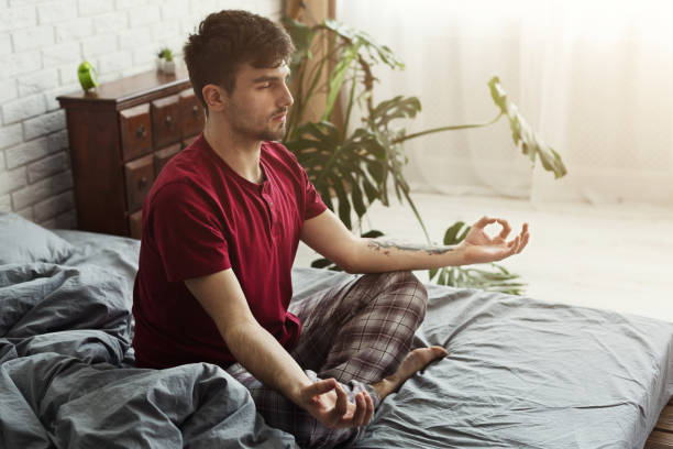 istock Young man sitting in bed in lotus pose 979131620