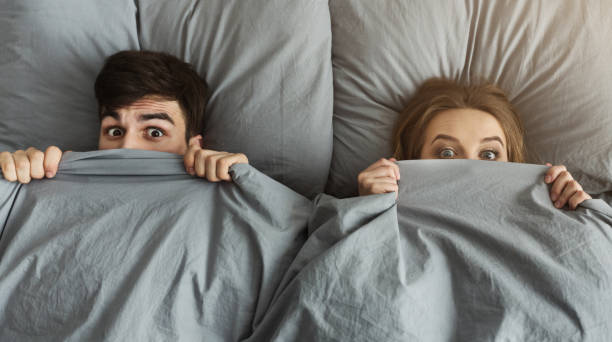 shocked man and woman hiding under blanket in their bed at home - men sensuality photography high angle view imagens e fotografias de stock