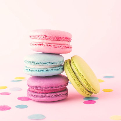 Stacking sweet colorful macarons on pink background decorated with confetti.