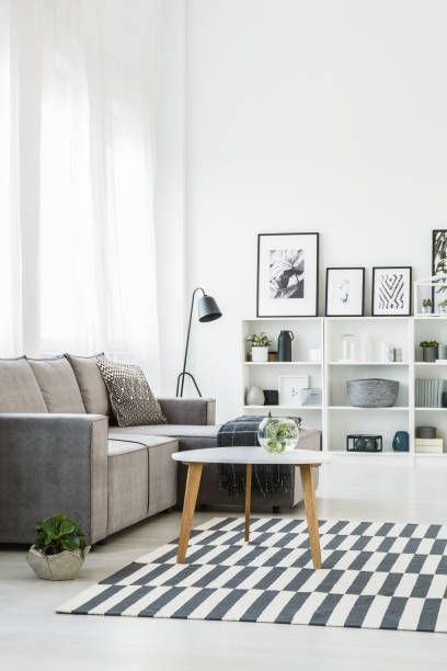 istock Table on patterned carpet in modern living room interior with grey sofa and posters. Real photo 979189526