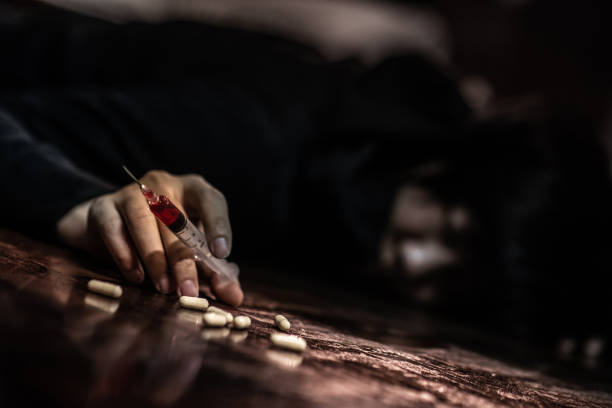 наркоман человек, л�ежащий на полу, держа в руках шприц для инъекций наркотиков и таблетки. смерть от передозировки наркотиков и наркомании � - narcotic teenager cocaine drug abuse стоковые фото и изображения