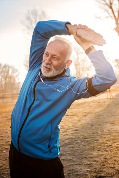 Mature man stretching arms in public park stock photo