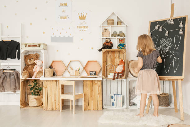 dziewczynka rysująca na tablicy w swoim pokoju z drewnianymi pudełkami, pluszowymi misiami i naklejkami ściennymi - childrens furniture zdjęcia i obrazy z banku zdjęć
