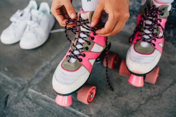 A picture of girl lying laces on her pink rollers. She has changed her white shoes to this funny rollers. Girl is almost ready to rollerblading