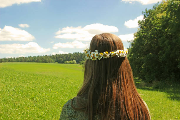 Elementary child waits in the park for a butterfly.  She wears purple flowers in her hair to dress up as 'mother nature'.