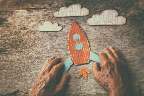 a close-up de um homem idoso segurando um foguete de papel em uma mesa de madeira. conceito de pensar sobre os sonhos de infância, a tristeza e a solidão - distress rocket - fotografias e filmes do acervo