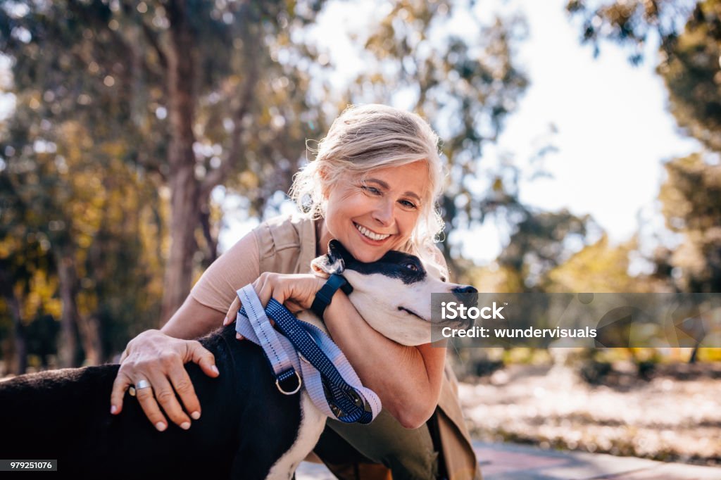 Affectionate mature woman embracing pet dog in nature Happy senior woman enjoying walk in nature and embracing pet dog in forest park Dog Stock Photo