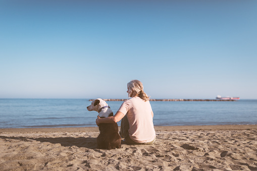 Mature woman with gray hair relaxing on beach with dog