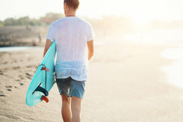 surfista em t-shirt branca andando com prancha de surf - wave salt surf sea - fotografias e filmes do acervo