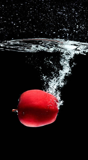 istock close up view of red apple falling into water isolated on black 979303948