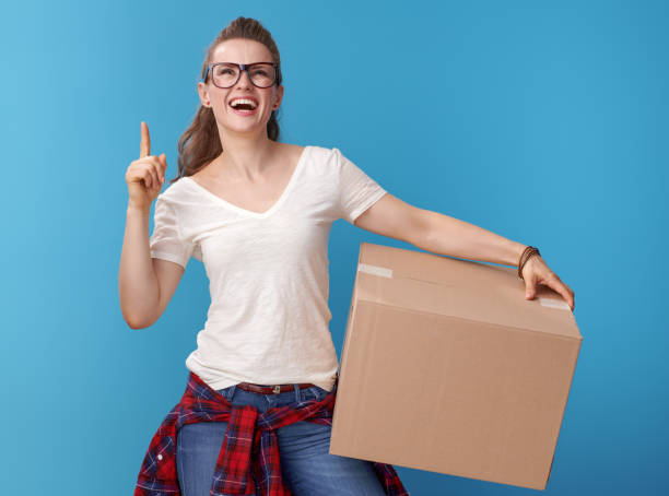 istock woman with cardboard box pointing up at copy space on blue 979305534