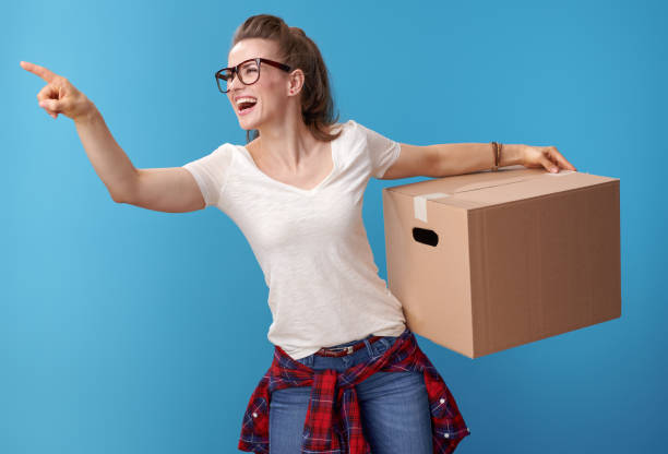 istock happy woman with cardboard box pointing at something on blue 979305632