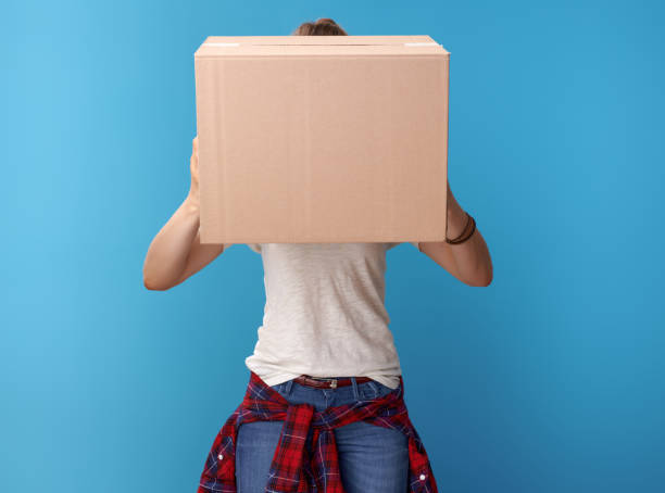 istock young hipster holding cardboard box in front of face on blue 979306128