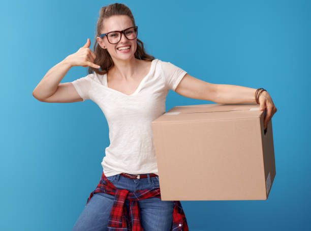 istock woman with cardboard box showing call me gesture on blue 979307280