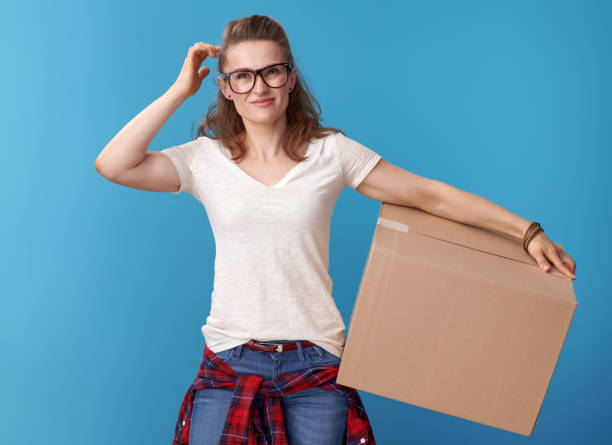 istock pensive young woman in white shirt with cardboard box on blue 979308564