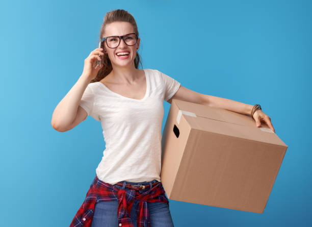 istock smiling woman with cardboard box talking on cell phone on blue 979312912