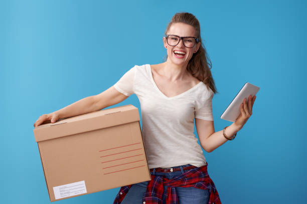 istock smiling woman with cardboard box and tablet PC on blue 979313140