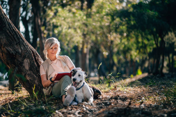 senior mujer relajante en la naturaleza con libro y mascota perro - women book mature adult reading fotografías e imágenes de stock