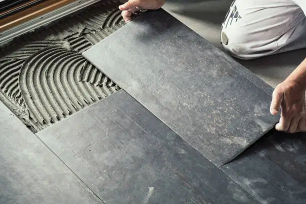 Worker carefully placing ceramic floor tiles on adhesive surface