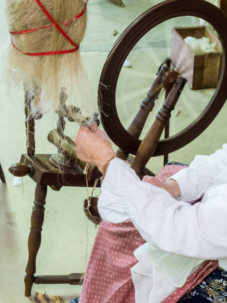 рабочие руки - ремесленник спиннинг шерсти, чтобы сделать нить с помощью старого деревянного вращающегося колеса, вертикальные - 5560 стоковые фото и изображения