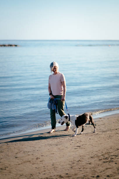 istock Happy active retired woman walking with pet dog on beach 979351798