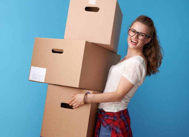 istock happy modern woman holding stack of cardboard boxes on blue 979356020