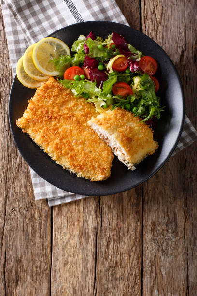 istock Fried fish fillet in breading and fresh vegetable salad close-up. Vertical top view 979356540