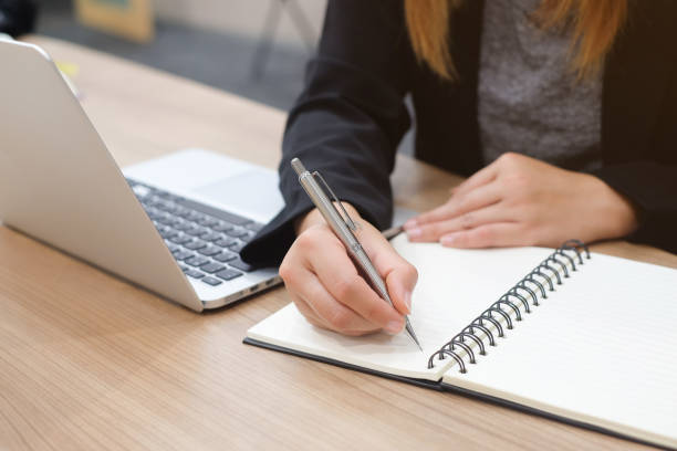 istock close up businesswoman hand writing content or somethings on notebook with using laptop at wooden table at office , work concept 979371126
