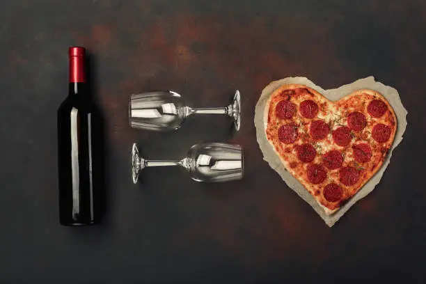 Heart shaped pizza with mozzarella, sausagered , wine bottle and two wineglass. Valentines day greeting card. Top view