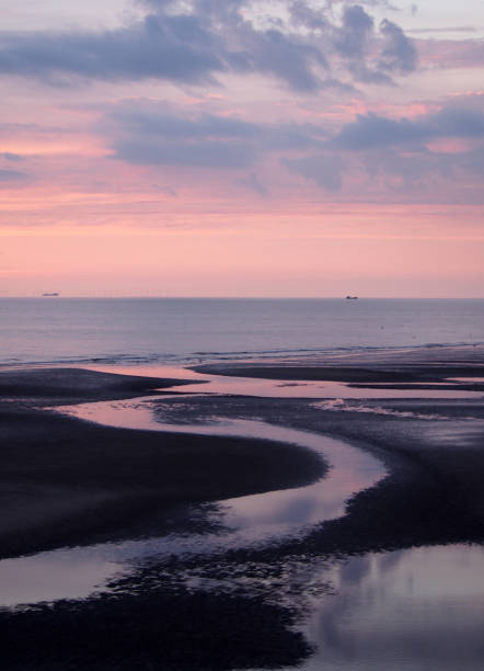 hermoso crepúsculo púrpura sobre un mar tranquilo con agua en la playa que reflejan nubes de atardecer coloridas - horizon over water england uk summer fotografías e imágenes de stock