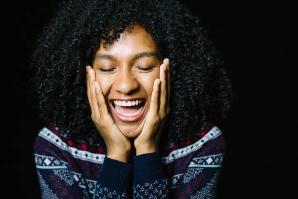 Close-up of happy young woman screaming. Female is with head in hands. She is having curly hair over black background.