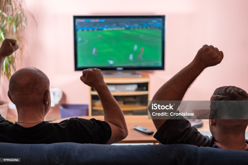 Father and son watching football or soccer on a TV. Father and son watching football or soccer on a TV and cheering. Soccer Stock Photo