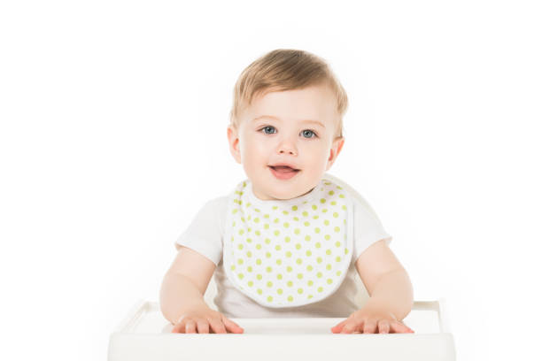 smiling baby boy in bib sitting in highchair isolated on white background smiling baby boy in bib sitting in highchair isolated on white background baby bib stock pictures, royalty-free photos & images