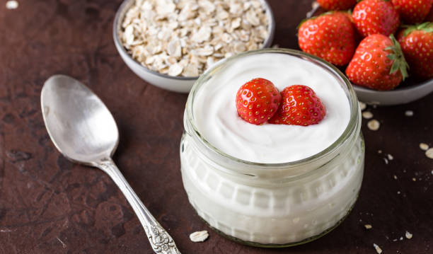 istock White yogurt in glass bowl with spoon and starwberries on rustic background. 979473572
