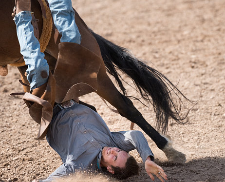 Rodeo cowboy falling off horse