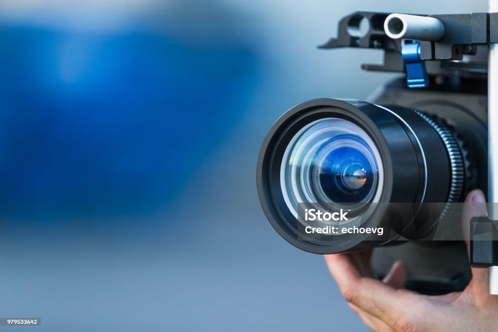 Camera lens attached to a camera and hand focusing close up detailed with smooth blue background and sunset reflections. Concept for videography cinematography vlogging video television movies making Television Camera Stock Photo