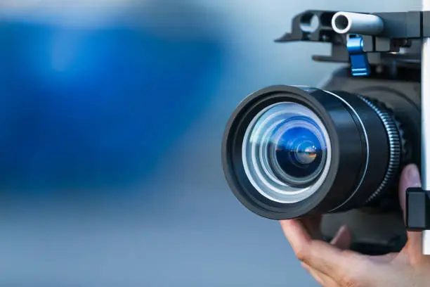 Photo of Camera lens attached to a camera and hand focusing close up detailed with smooth blue background and sunset reflections. Concept for videography cinematography vlogging video television movies making