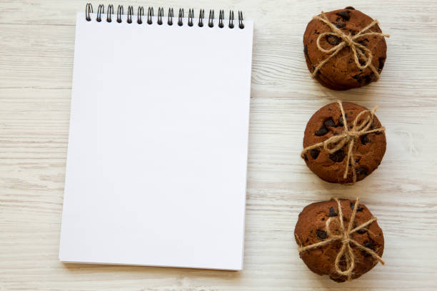 istock Chocolate chip cookies with notebook on a white wooden table, from above. Top view. 979563110