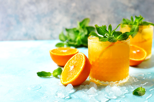 Cold summer orange lemonade with mint and ice cubes in a glass.
