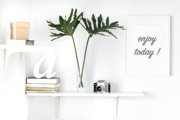 istock Home interior with mock up frame, retro photo camera, books and modern green leafs. Shelf concept in scandi interior. 979566262