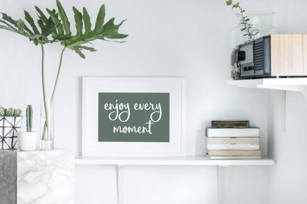 istock Stylish scandi interior with white shelf, mock up frame, books, radio and leafs. 979566302