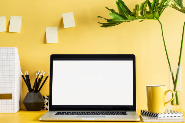 istock Stylish office workspace with laptop mock up screen, office accessories, leafs on the yellow wall. 979567630