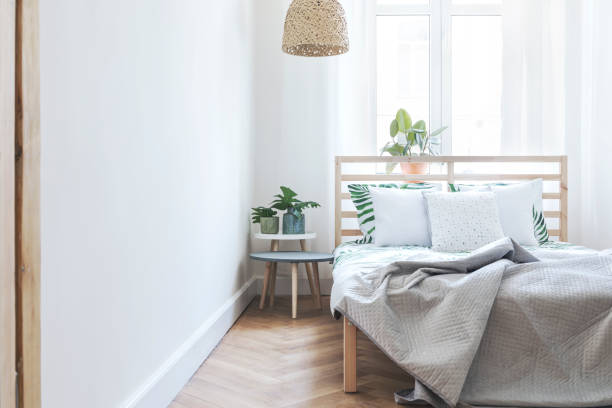 istock Modern scandinavian sunny bedroom with plants , floral pattern bedding and pilows. Space with white walls and brown wooden parquet. 979585128