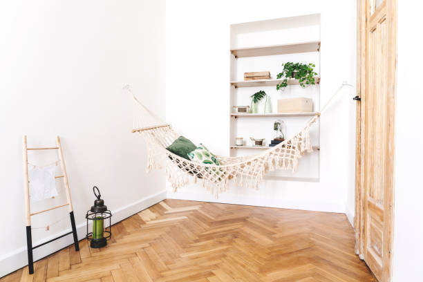 istock Modern and stylish bedroom with natural string hammock, plants and shelves with accessories. Bright and sunny bedroom with brown wooden parquet. 979585252