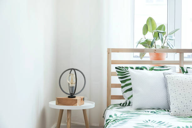 istock Modern and stylish bedroom with plants, design lamp and floral pattern bedding. Bright and sunny space with wooden parquet and white walls. 979585720